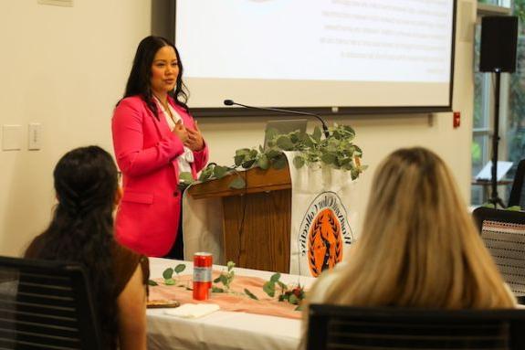 Woman in pink blazer speaks at podium 